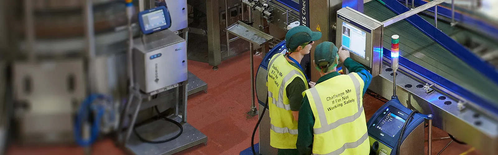 two employees in high vis gathered around domino screen above production line