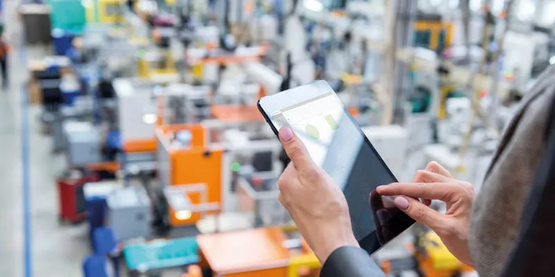 Overview of factory, hands holding tablet and using it with graphs on screen. 