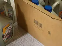 A group of car oil bottles inside a porous cardboard box with a Cx150i code printed on the outside.