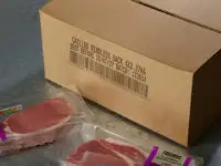 A porous cardboard box with a Cx150i code printed on the outside and some packets of bacon nearby.